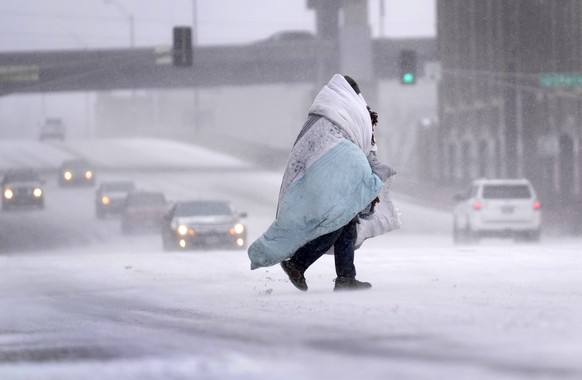 A person wrapped in a blanket crosses a snowy street on Thursday, December 12.  22, 2022, in St Louis.  Frigid air is moving eastward across the central United States, with windchill advisories for…