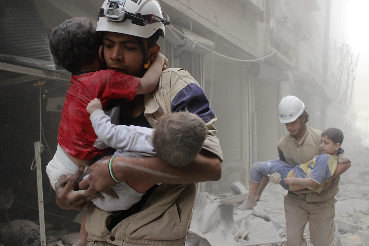 Mitglieder der Schutzbrigade retten Kinder aus einem von Bomben getroffenen Haus in Aleppo.