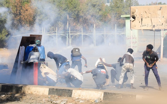 epa09676045 Sudanese protesters take cover as security forces fire tear gas during clashes with security forces at an anti-coup protest, in Khartoum, Sudan, 09 January 2022. Security forces fired tear ...