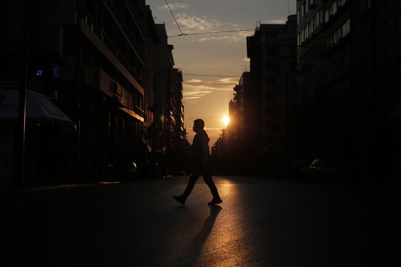 epa08822427 A pedestrian wearing a face mask is silhouetted against the setting sun as he crosses a street during the second lockdown of the country, to stem the spread of the coronavirus pandemic, in ...