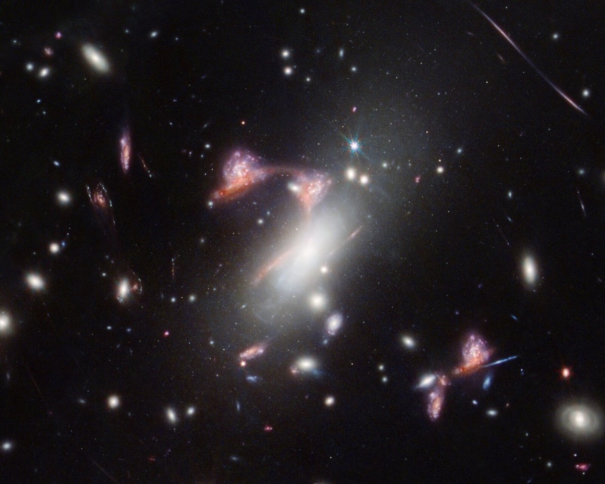 Thanks to a cosmic magnifying glass effect, the gravity of a massive galaxy cluster is warping two distant interacting galaxies (a face-on spiral and a dusty red galaxy) behind it, making them appear  ...