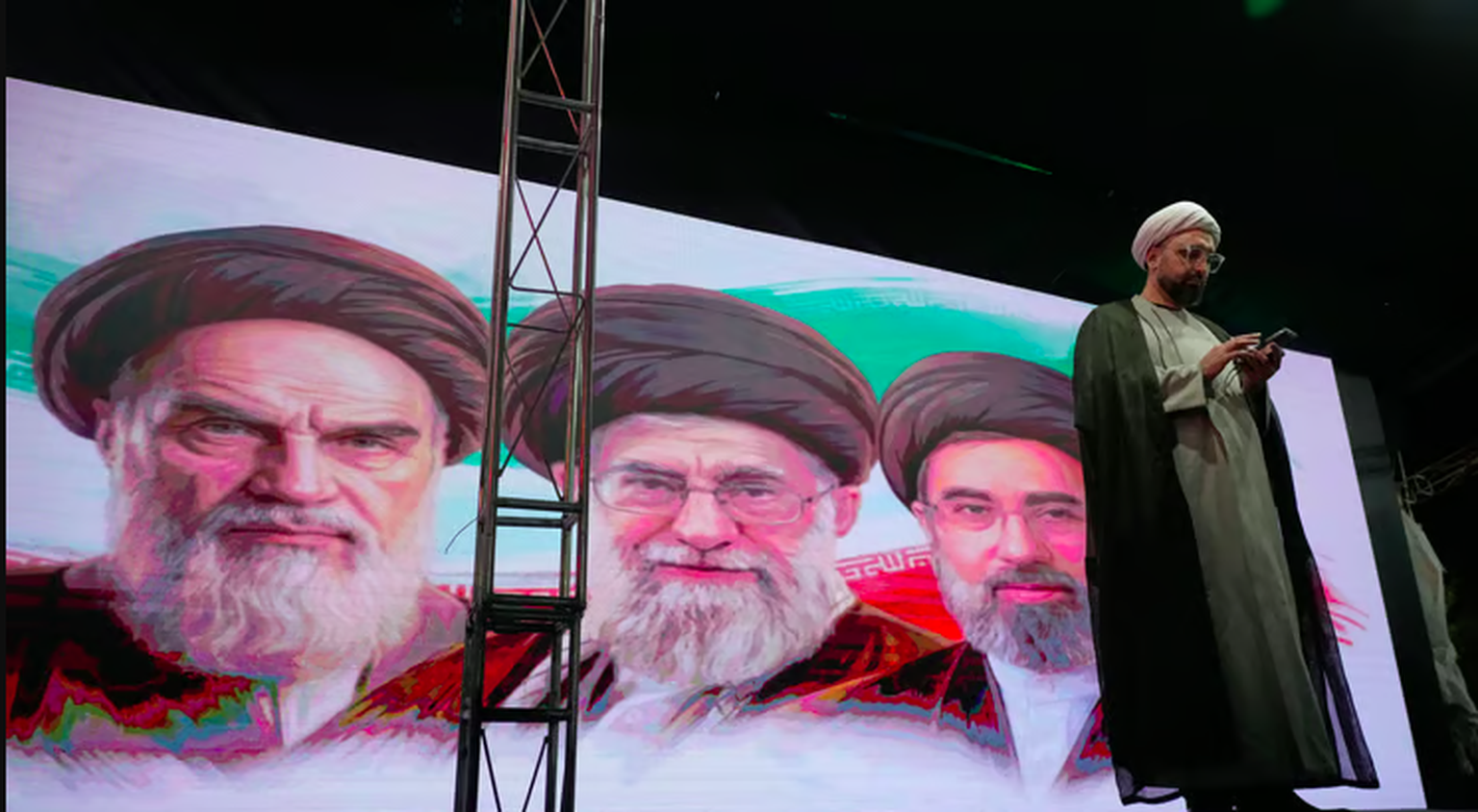 Vor den Porträts von Ruhollah Chomeini, Ali Khamenei und Modschtaba Khamenei nutzt ein Geistlicher sein Mobiltelefon während einer regimetreuen Kundgebung in Teheran.