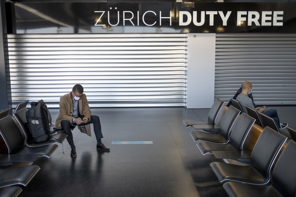 epa09091913 Passengers wearing face masks wait before boarding an airplane in front of a closed Zuerich Duty Free shop at the Zuerich Airport (Flughafen Zuerich) amid the coronavirus disease (COVID-19 ...