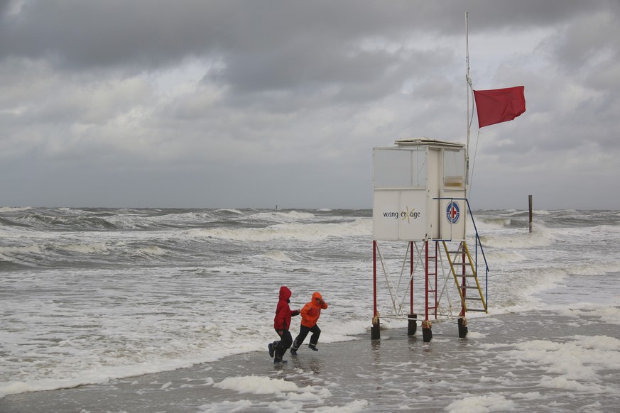 Kinder laufen am 05.10.2017 auf dem Strand von Wangerooge (Niedersachsen) bei stürmischen Wind vor den Wellen davon. (KEYSTONE/DPA/Peter Kuchenbuch-Hanken)