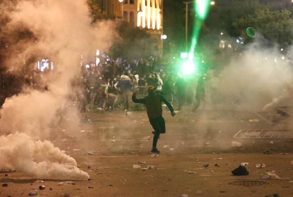 An anti-government protester throws stones against the riot police, during a protest near the parliament square, in downtown Beirut, Lebanon, Sunday, Dec. 15, 2019. Lebanese security forces fired tear ...