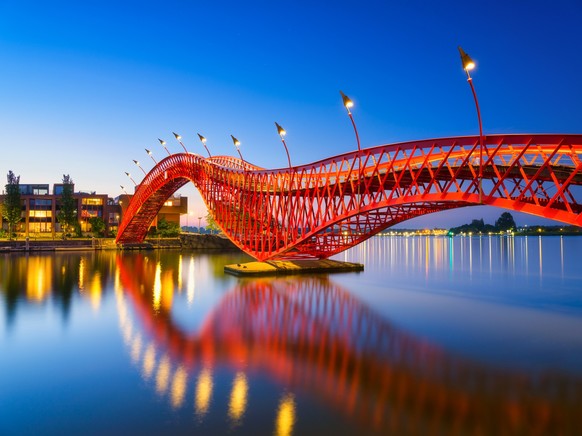 A bridge in the city at night.  The bridge on the blue sky background during the blue hour.  Architecture and design.  The Python Bridge, Amsterdam, Netherlands.