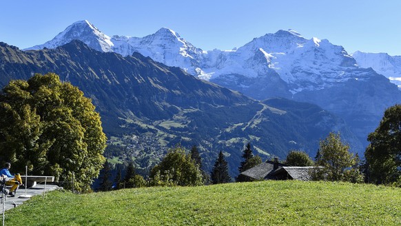 Personen geniessen auf einer Terasse das schoene Herbstwetter mit Blick auf das Dreigestirn Eiger, Moench und Jungfrau, von links, am Sonntag, 16. Oktober, in Sulwald ob dem Lauterbrunnental. (KEYSTON ...