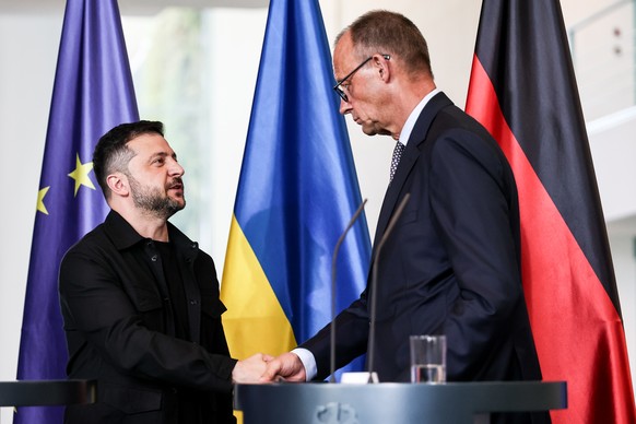 epa12297937 German Chancellor Friedrich Merz (R) and Ukrainian President Volodymyr Zelensky shake hands after a press conference following a video call with other heads of state ahead of a summit betw ...