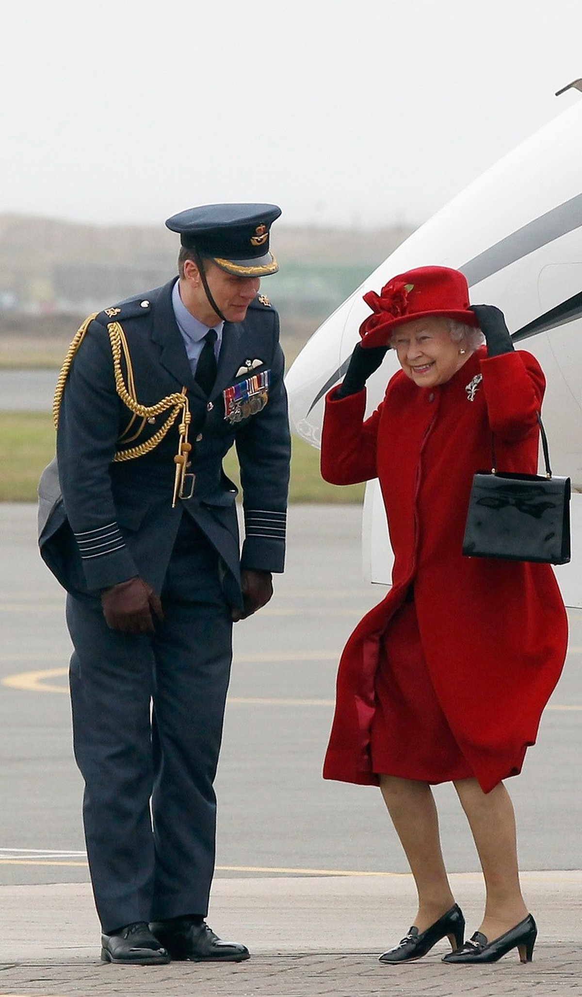 Britain's Queen Elizabeth II holds on to her hat in high winds as she is greeted by Group Captain Bruce Headley during a visit to RAF Valley, Anglesey, Wales, where her grandson Prince William, i ...