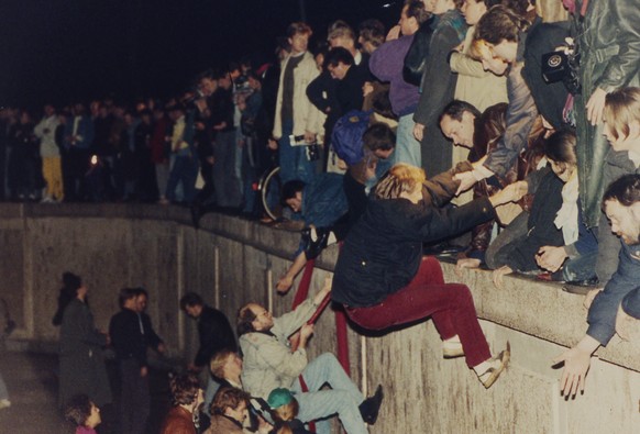 ARCHIVE --- VORSCHAU 30. JAHRESTAG MAUERFALL BERLIN AM 9. NOVEMBER 2019 --- East Berliners get helping hands from West Berliners as they climb the Berlin Wall which has divided the city since the end  ...