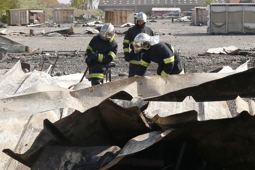 epa05902704 Firefighters working amongst the remains of burnt huts at the Grande-Synthe migrant camp outside the northern French city of Dunkirk on 11 April 2017 after a blaze destroyed the camp late  ...