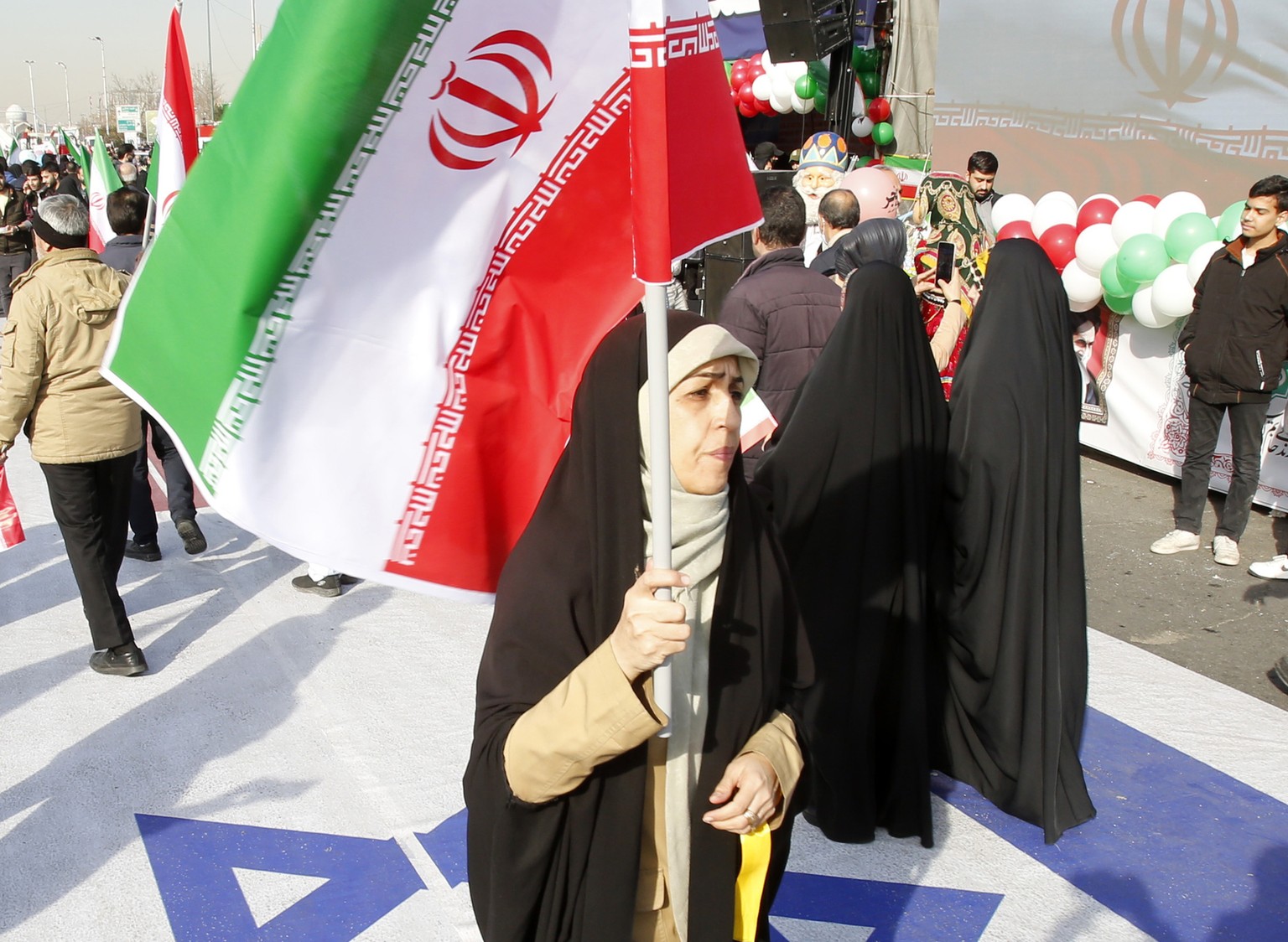 epa11144361 An Iranian woman holds Iran&#039;s national flag as she walks on Israel&#039;s flag during the 45th anniversary of the Islamic Revolution in Tehran, Iran, 11 February 2024. Iran celebrates ...