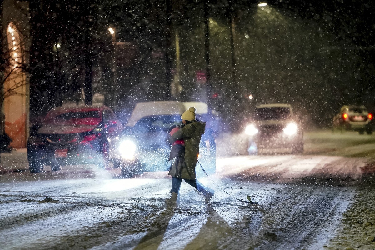 A person carries their dog as they cross Butler Street as snow falls during a winter storm that will impact the region on Sunday night, Jan. 16, 2022, in Lawrenceville a neighborhood in Pittsburgh. (A ...