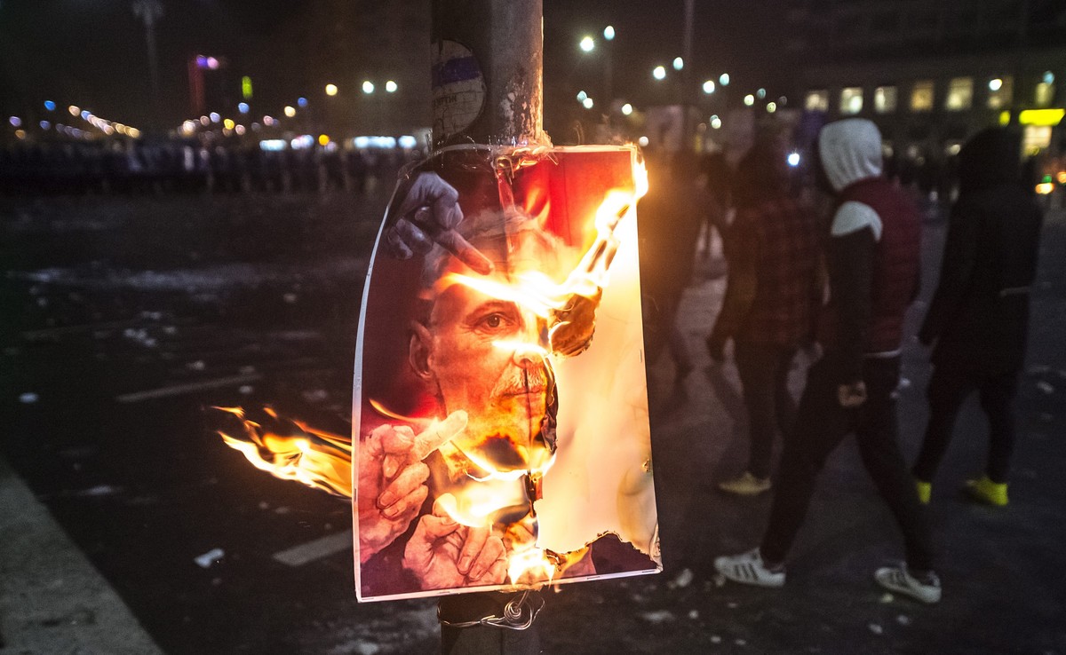 epa05765724 Masked protesters pass a burning poster during a protest rally in front of government headquarters in Bucharest, Romania, early 02 February 2017. Up to 100,000 people gathered peacefully i ...