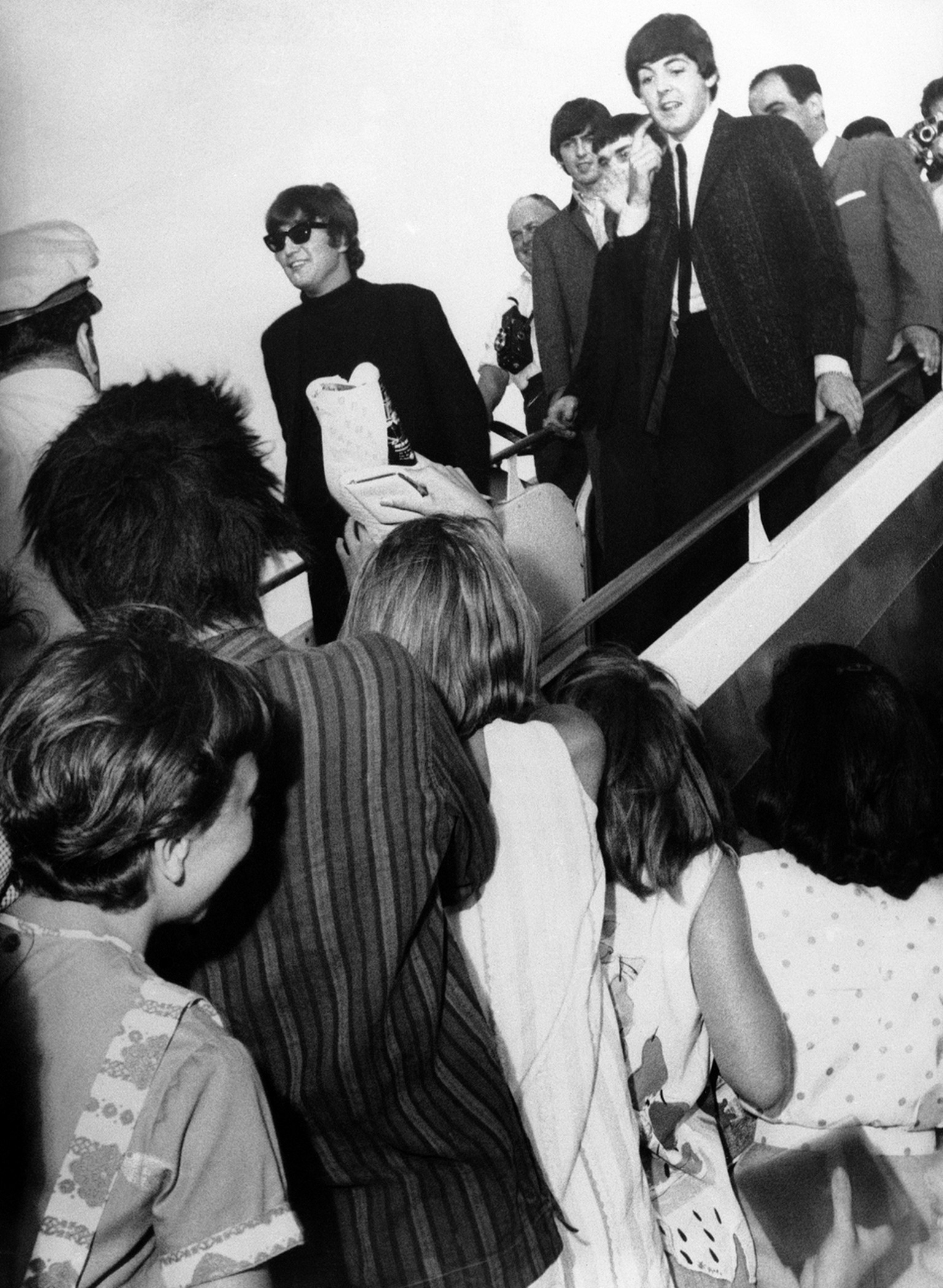 Die Beatles auf einem Zwischenstopp in Beirut auf dem Weg nach Hongkong. Zahlreiche Fans waren zum Flughafen gekommen und verlangten, die Stars zu Gesicht zu bekommen. John Lennon, George Harrison, Jimmy Nicol (der für den erkrankten Ringo Starr eingesprungen war) und Paul McCartney zeigten sich kurz und verschwanden dann wieder in ihrem Flugzeug. So gross war der Andrang (siehe Bild unten), dass die Flughafenpolizei die Menge schliesslich mit Wasserwerfern vertrieb (07.06.1964).<br>