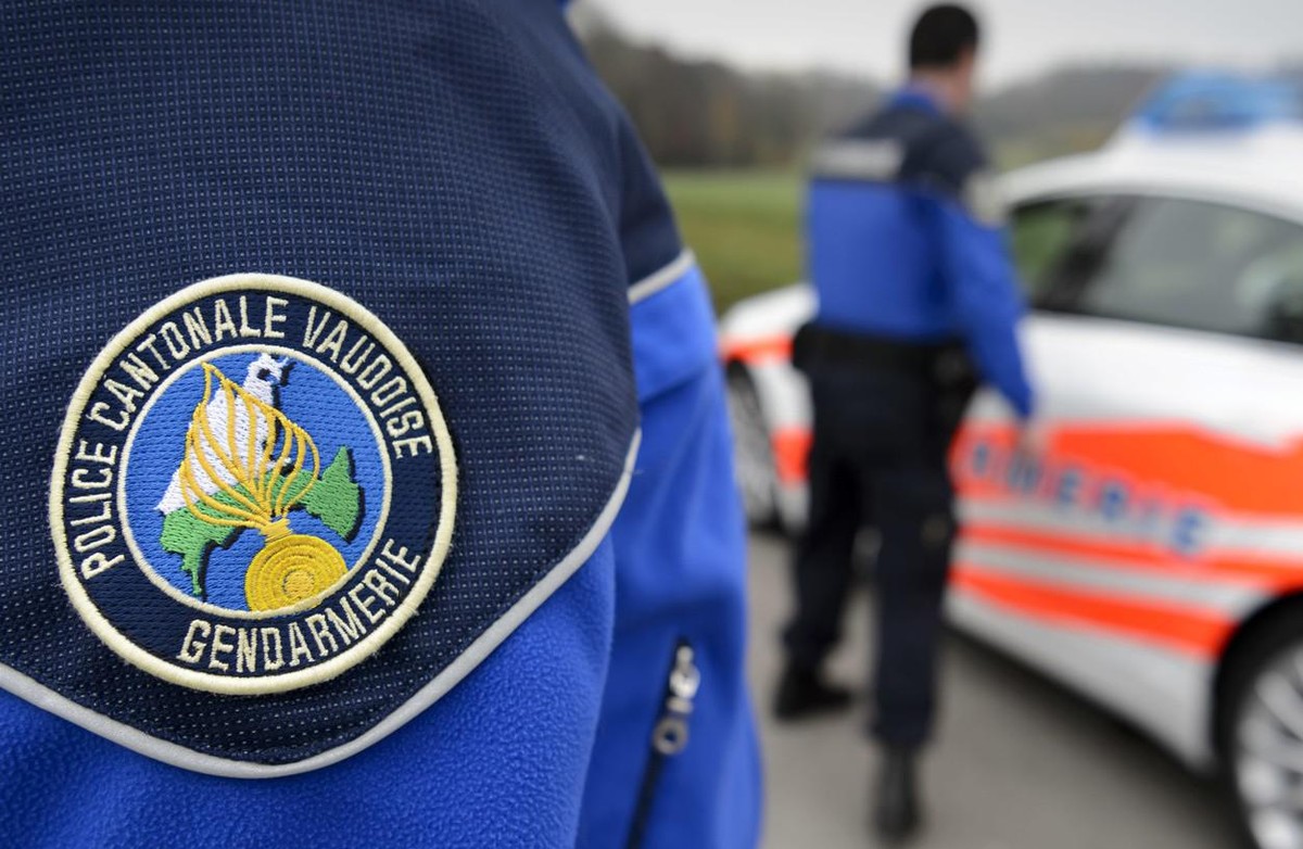 [Editor's note: photo mise-en-scene] Detail view of the uniform of a police officer of the cantonal police of Vaud, in the foreground, and another cantonal police officer next to a police car, in ...