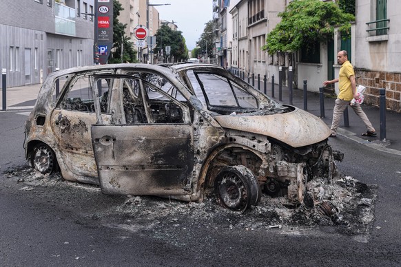 epa10720366 A person walks near the remains of a burnt out car following a night of looting and rioting in Montreuil, near Paris, France, 01 July 2023. Violence broke out across France over the fatal  ...