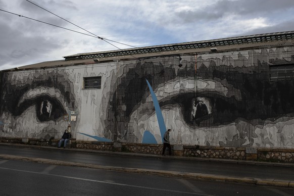 Two men wearing face masks to prevent the spread of the coronavirus walk past a giant mural by Greek street artist iNO depicting the eyes of Leonardo da Vinci&#039;s Mona Lisa, in Athens, Thursday, De ...