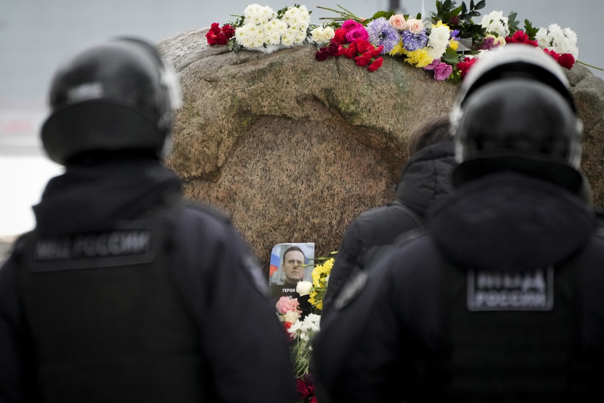 Police officers watch as people lay flowers paying the last respect to Alexei Navalny at the monument, a large boulder from the Solovetsky islands, where the first camp of the Gulag political prison s ...