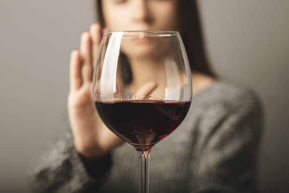 Frau hinter Weinglas will keinen Alkohol trinken.