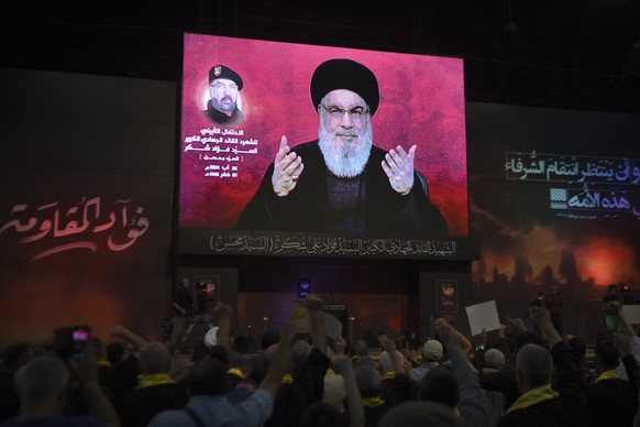 Supporters raise their fists and cheer as they watch a speech given by Hezbollah leader Sayyed Hassan Nasrallah on a screen during a ceremony to commemorate the death of top commander Fouad Shukur, wh ...