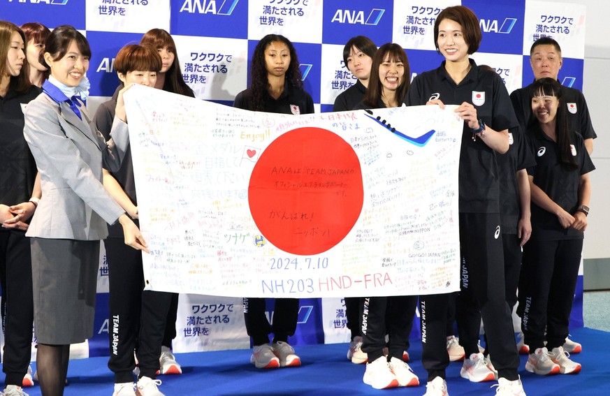 July 10, 2024, Tokyo, Japan - Japanese women s volleyball team captain Sarina Koga R and her teammates receives Japanese national flag from an All Nippon Airways ANA cabinattendant before they leave t ...