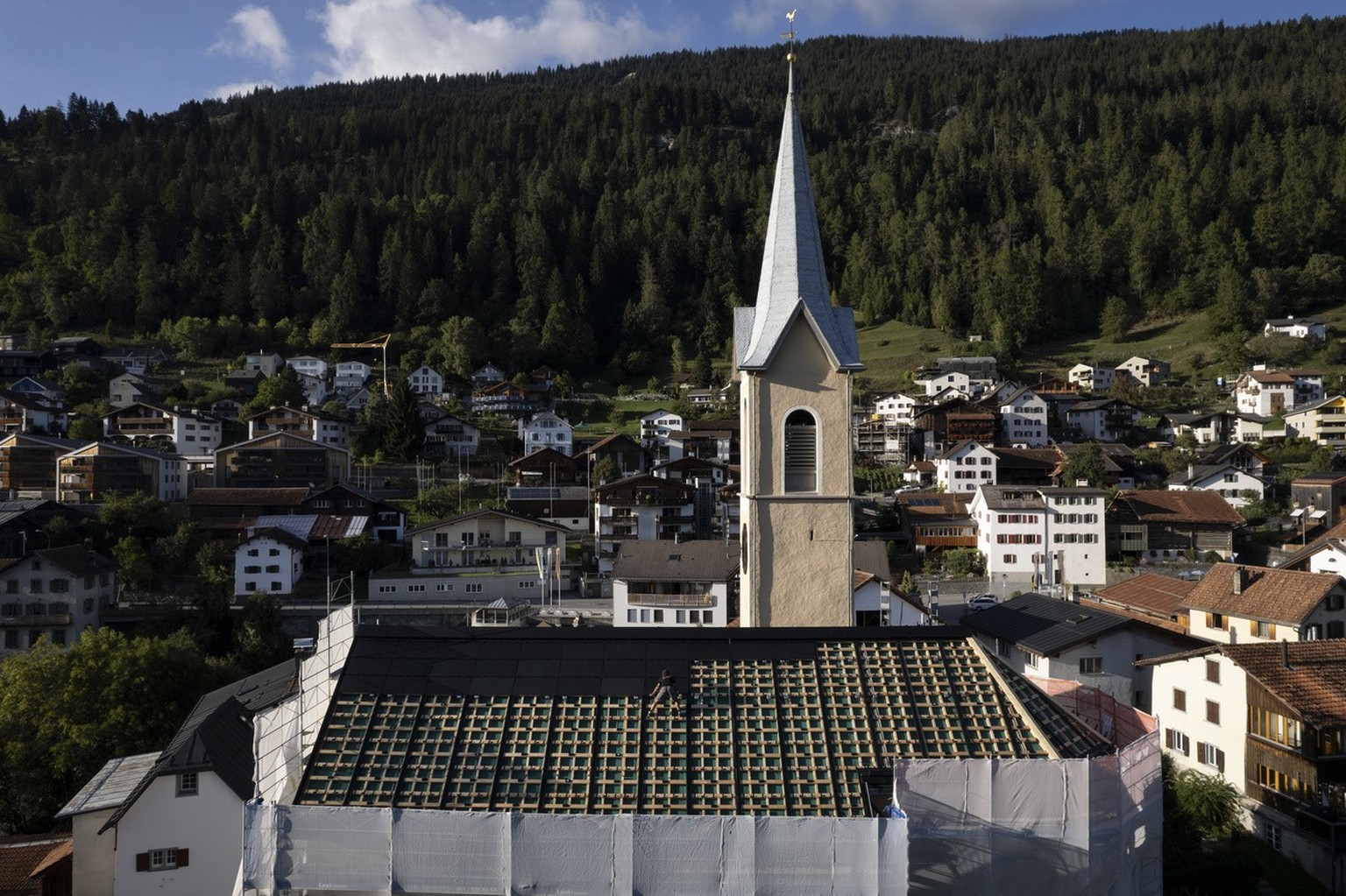 Arbeiter montieren Solarpanels auf dem Dach der historischenKirche, aufgenommen am Dienstag, 19. September 2023, in Trin. (KEYSTONE/Gian Ehrenzeller)