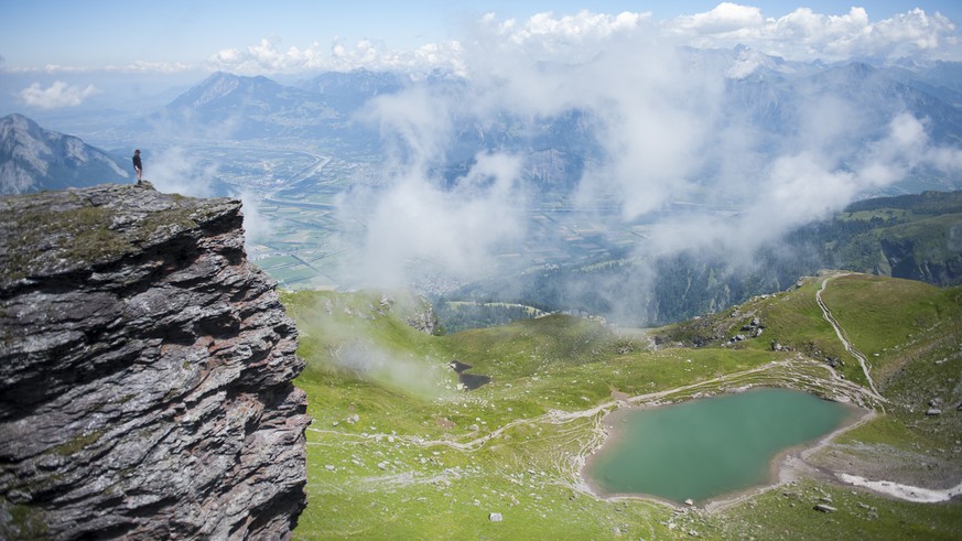 Eine Wanderin blickt von einem Felsvorsprung ueber das St. Galler und Churer Rheintal, unter ihr der Baschalvasee, auf der Fuenf Seen Wanderung, am Mittwoch, 16. Juli 2014, in Wangs-Pizol. (KEYSTONE/G ...