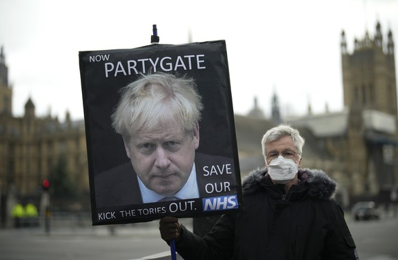 FILE - An anti-Conservative Party protester holds a placard with an image of British Prime Minister Boris Johnson including the words &quot;Now Partygate&quot; backdropped by the Houses of Parliament, ...