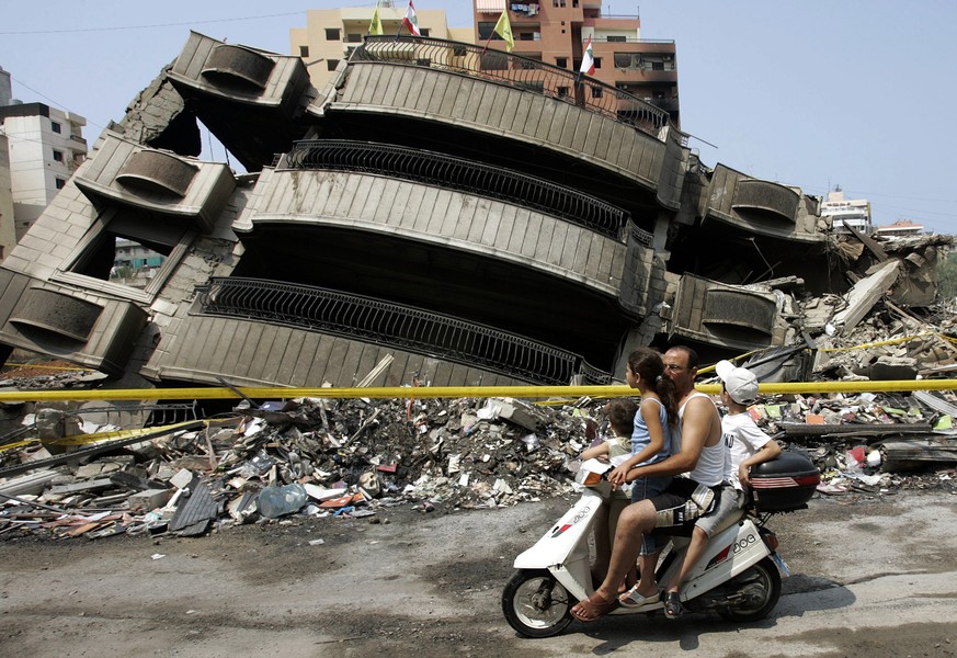 File - In this August 20, 2006 file photo, a Lebanese man with his three children, riding a scooter pass in front of a destroyed building that was attacked during the 34-day long Hezbollah-Israeli war ...