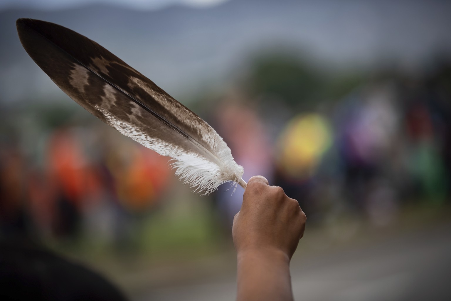A woman holds an eagle feather while watching a convoy of truckers and other vehicles travel past in support of the Tk'emlups te Secwepemc people, after the remains of 215 children were discovered bur ...