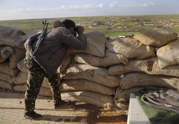 FILE - A fighter from the U.S-backed Syrian Manbij Military Council looks through binoculars towards Turkish-backed fighters&#039; positions, at the front line at the village of Halawanji, north of Ma ...