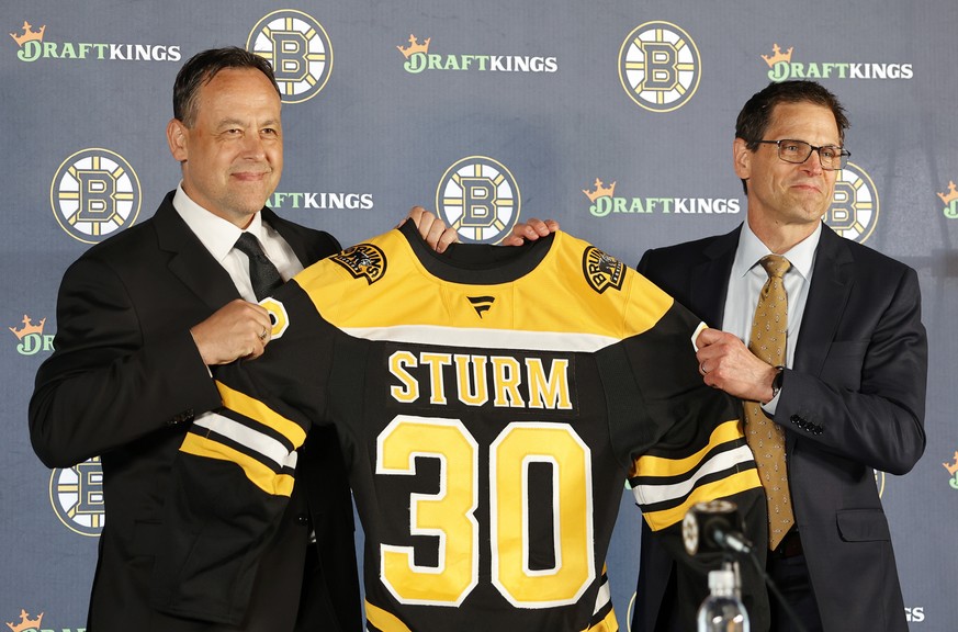 Boston Bruins new head coach Marco Sturm, left, smiles as he is presented a jersey by general manager Don Sweeney during an NHL hockey news conference, Tuesday, June 10, 2025, in Boston. (AP Photo/Mar ...