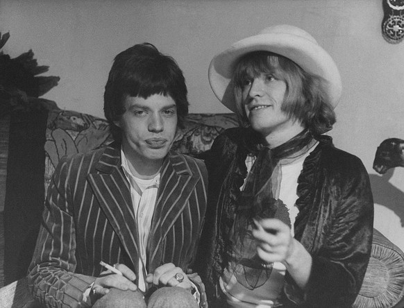 British singer and musician Mick Jagger (Michael Phillip Jagger) sitting beside British guitarist and multi-instrumentalist Brian Jones wearing woman clothes. The two are founding members of British b ...