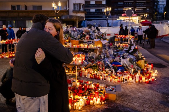 KEYPIX - People react as flowers and candles are pictured in tribute to the victims on the site of the fire at the 'Le Constellation' bar and lounge, in Crans-Montana, Switzerland, on Saturd ...