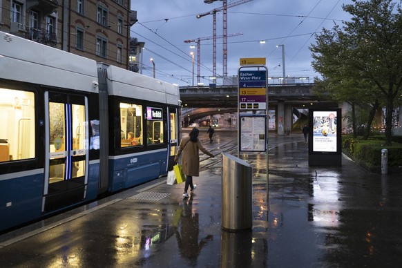 Passanten gehen auf dem Trottoir neben einem beleuchteten digitalen Werbeschild, bei Regenwetter, in der Abenddaemmerung, fotografiert bei Escherwyssplatz am Mittwoch, 12. April 2023 in Zuerich. (KEYS ...