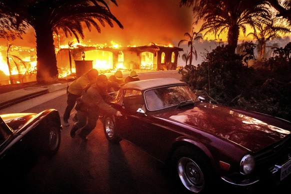 Firefighters and sheriff&#039;s deputies push a vintage car away from a burning home as the Mountain Fire burns in Camarillo, Calif., Nov. 6, 2024. (AP Photo/Noah Berger)