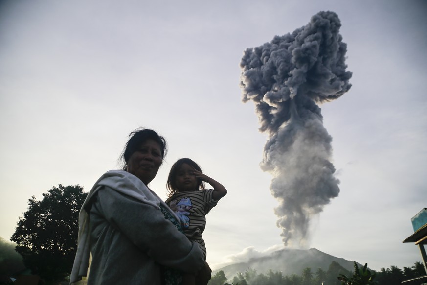 epaselect epa11826439 A woman carries a child as Mount Ibu spews volcanic material up to the sky in the background during the eruption in West Halmahera, North Maluku province, Indonesia, 15 January 2 ...