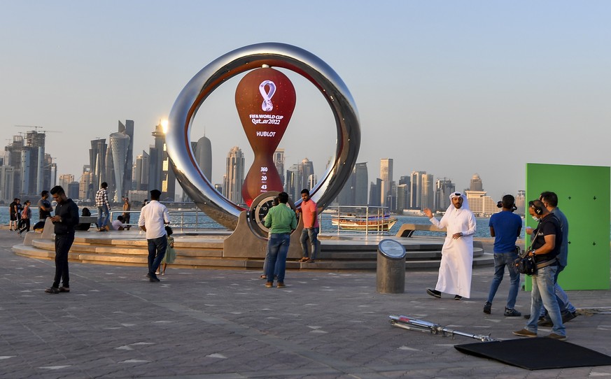 epa09603273 People pose in front of the clock counting down to the first match of the FIFA World Cup 2022 at Doha Corniche in Doha, Qatar, 25 November 2021. The FIFA World Cup 2022, the first to be he ...