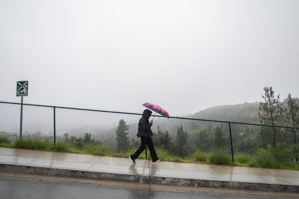 A tourist walks on the rain near the Hollywood sign that has the view blocked by clouds and heavy rain on December 24, 2025 in Los Angeles, California. A major winter storm rolled into California on D ...
