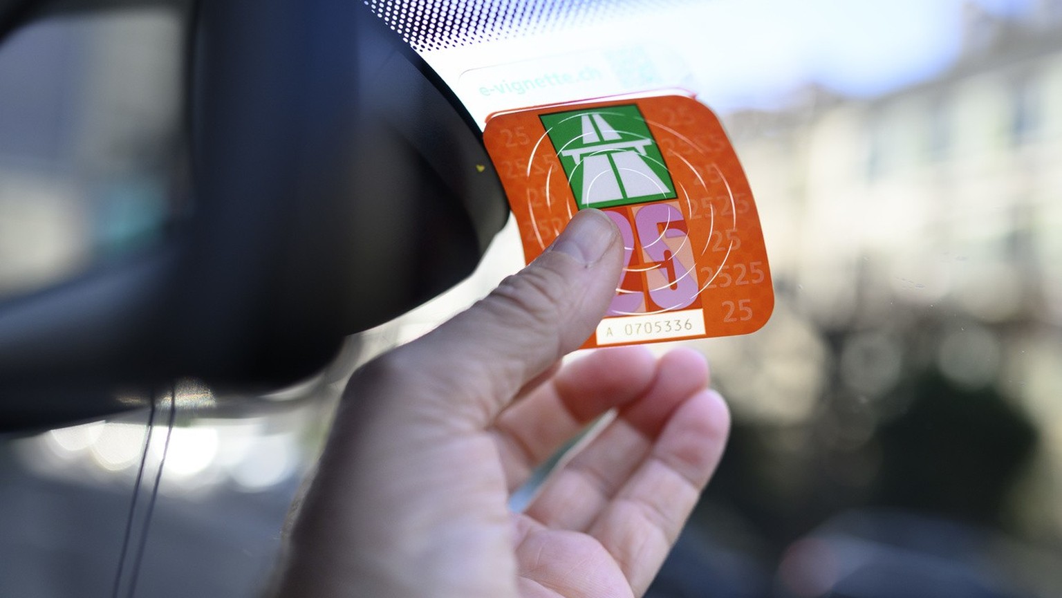 Ein Mann klebt eine Autobahnvignette fuer das Jahr 2025 auf die Windschutzscheibe eines Autos, fotografiert am Freitag, 6. Dezember 2024 in Bern. (KEYSTONE/Christian Beutler)