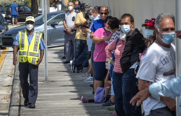 epa08432547 A Miami Police officer guards the line of the people who are going to receive bags of hot food, cooked in local restaurants, in Little Havana, Miami, Florida, USA, 19 May 2020. In order to ...