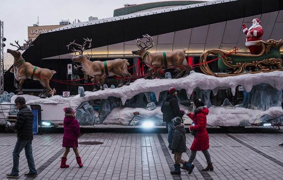 People walk by a Santa Claus statue in the Quartier des Spectacles on Christmas Day in Montreal, Friday, Dec. 25, 2020. Pedestrians took some time to enjoy the Christmas cheer as the province goes int ...