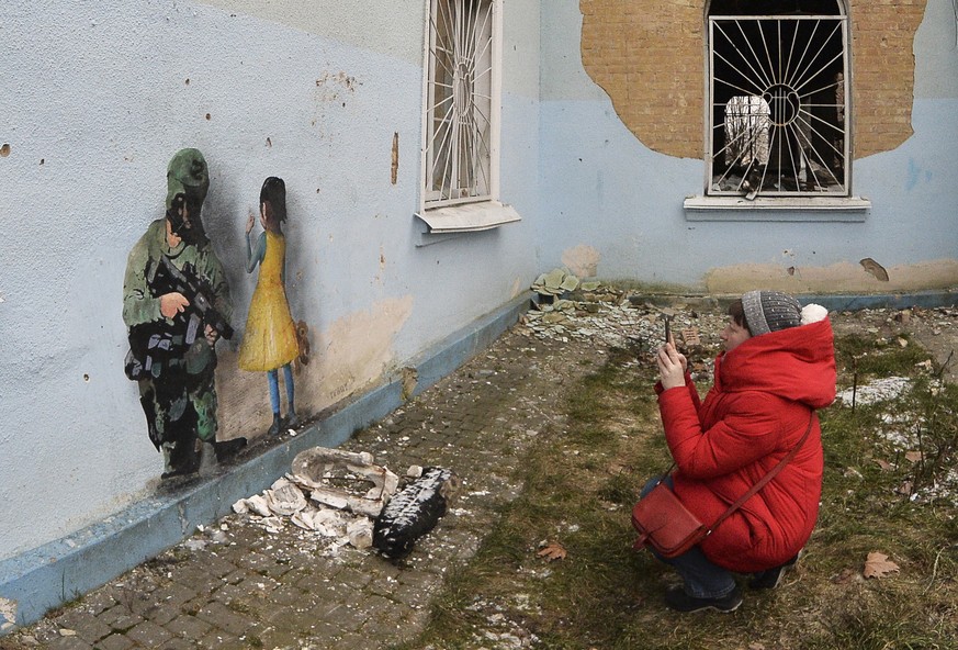 epa10436345 A woman photographs a graffiti signed by TVBOY on a wall of a damaged cultural center in the city of Irpin, near Kiev, Ukraine January 28, 2023 during the Russian invasion.  TVBOY is the pseudo...
