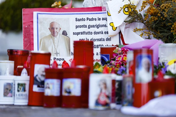 epa11954986 People leave candles and cards at the base of the statue of John Paul II at the entrance to the Gemelli Hospital, where Pope Francis is hospitalized, in Rome, Italy, 11 March 2025. Pope Fr ...