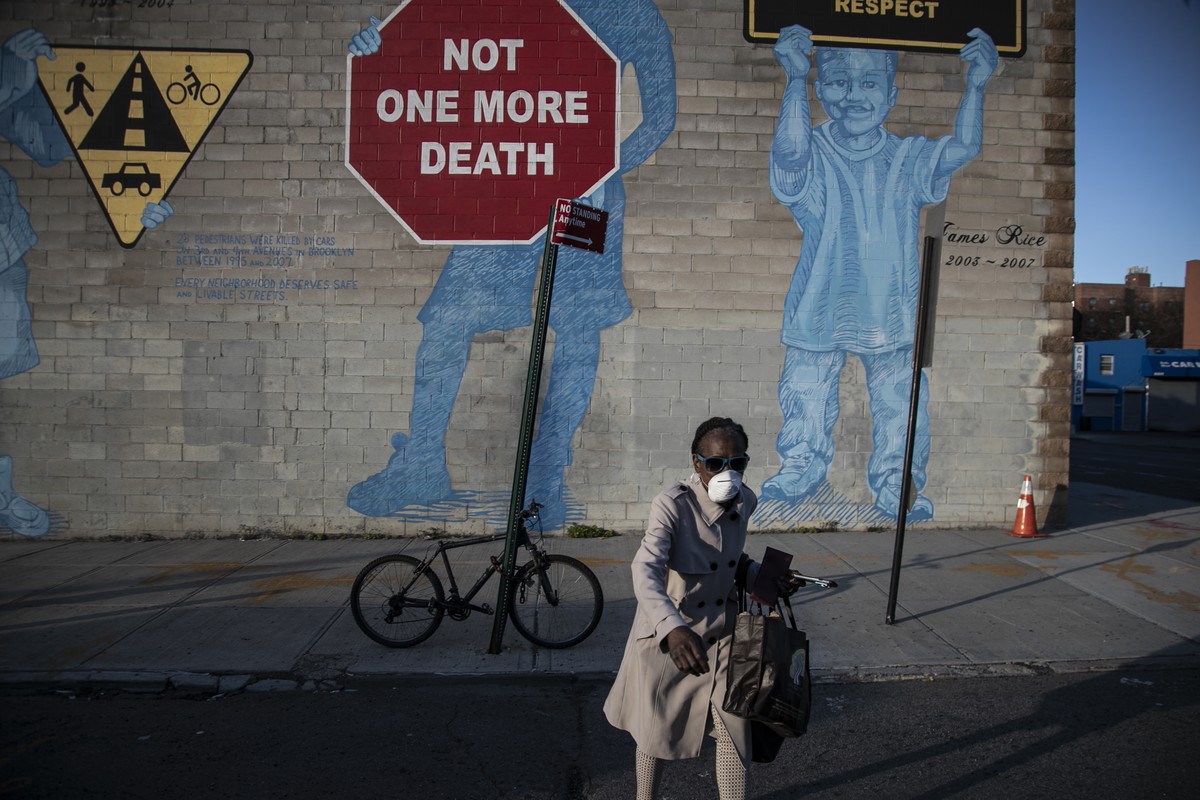 A woman wearing a mask crosses the street in front of a mural about traffic accidents reading, "NOT ONE MORE DEATH" in the Brooklyn borough of New York Friday, March 27, 2020. The new corona ...