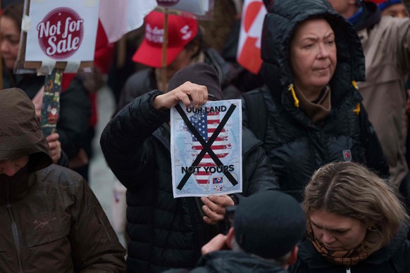 A man holds a map of Greenland covered in the American flag crossed out with an X during a protest against Trump's policy towards Greenland in front of the US consulate in Nuuk, Greenland, Saturd ...