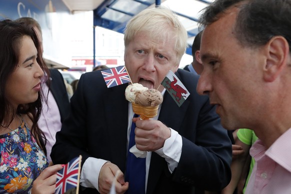 FILE - In this Saturday, July 6, 2019 file photo Conservative Party leadership candidate Boris Johnson, centre, eats an ice cream in Barry Island, Wales. (AP Photo/Frank Augstein, File)