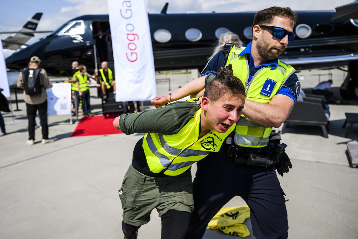 A police officer evacuates environmental activists of Stay Grounded and Greenpeace as they protest around a aircraft during the European Business Aviation Convention and Exhibition (EBACE), at the Gen ...