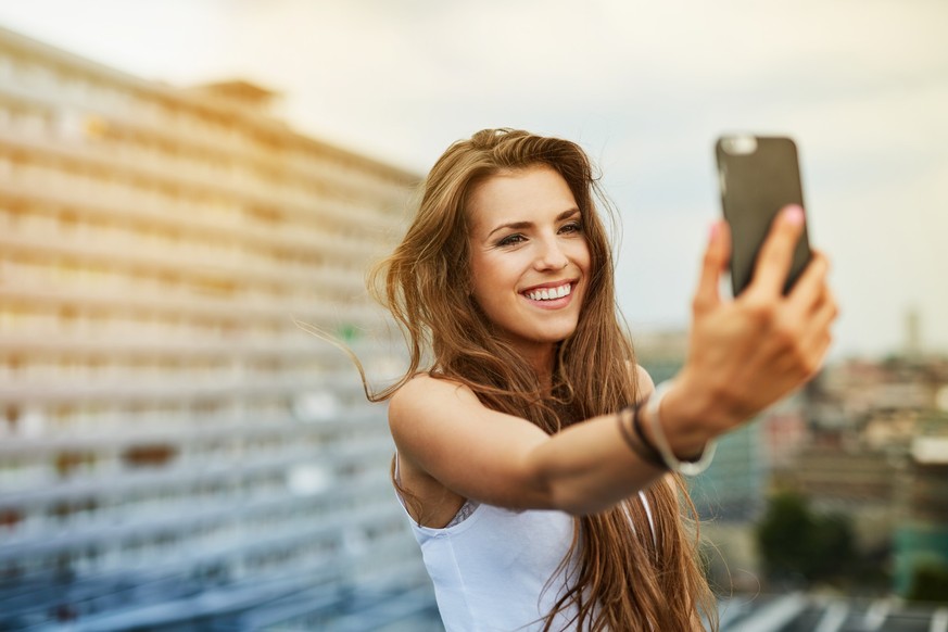 Eine junge Frau macht ein Selfie mit ihrem Smartphone.